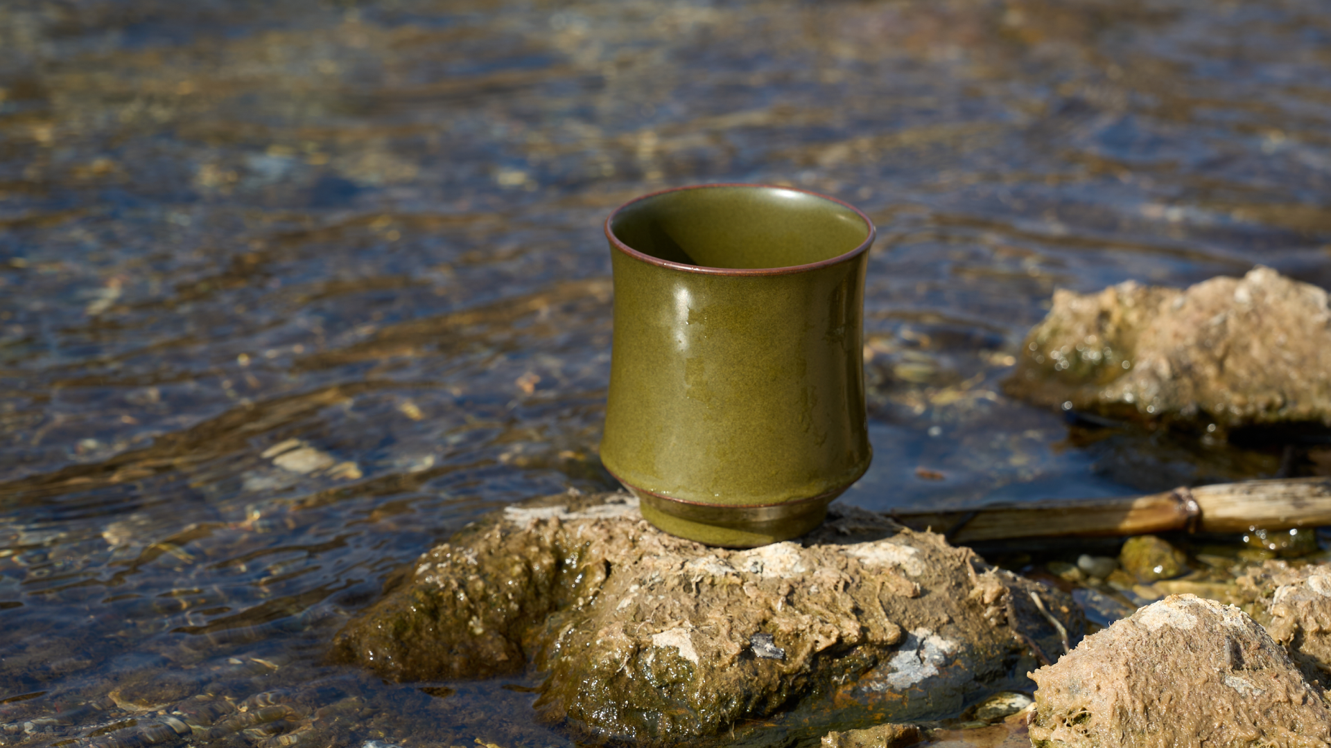 Tea-Dust Glaze Ceramic Cup with vintage matte finish, resting on a river rock surrounded by shimmering water. Capturing the Zen-inspired essence of the 72-step handcrafted Jingdezhen porcelain ritual.