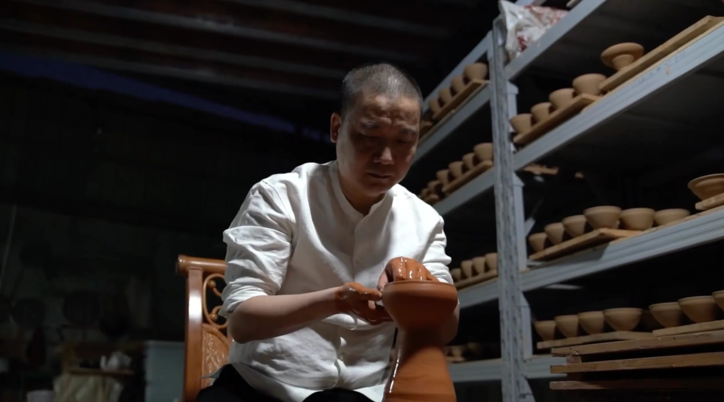 A master potter in a white shirt skillfully shapes a clay cup for Saragaia Jingdezhen.