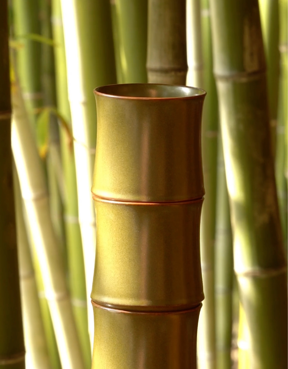 Handcrafted 72-step Tea-Dust Glaze bamboo branch mug resting naturally within a lush green bamboo forest. Capturing the Zen-inspired essence of artisan Jingdezhen porcelain artistry.