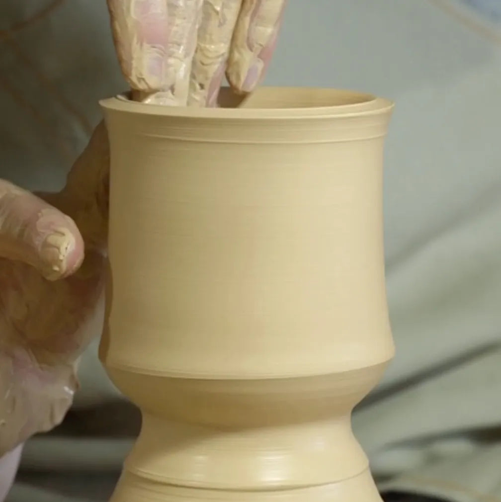 Close-up shot of a ceramic master shaping wet clay on a pottery wheel by hand to form a Saragaia bamboo-inspired cup structure.