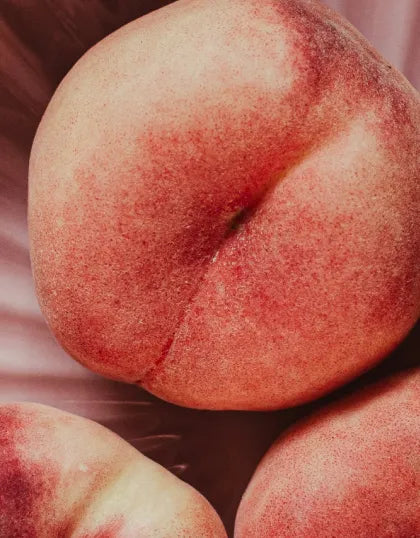 A close-up view of fresh ripe peaches with soft pinkish-red velvet skin, showcasing the organic peach blossom inspiration behind Saragaia's ceramic glaze collection.