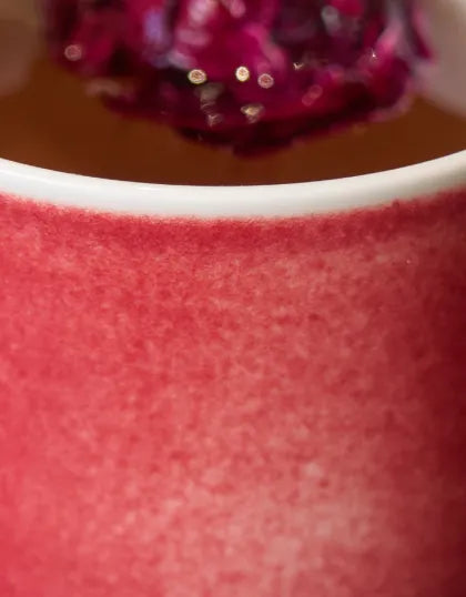 A close-up detail shot of a Saragaia ceramic cup edge, showing the rich texture of the vibrant red peach blossom glaze.