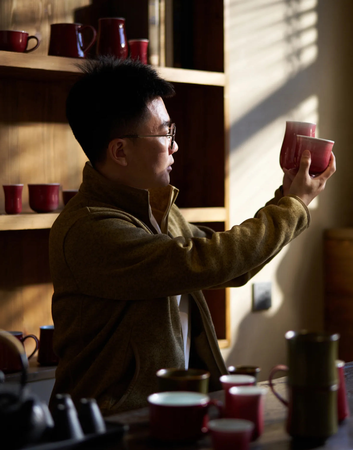 Saragaia founder examining handcrafted ceramic cups under soft natural light near a display shelf in the studio.