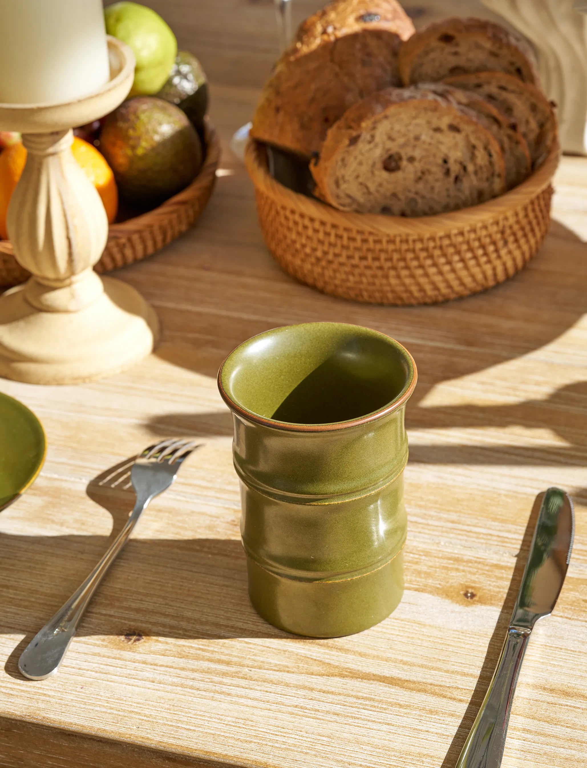 SaraGaia Tea-Dust Glaze tall bamboo-shaped porcelain cup on a sunny wooden breakfast table, accompanied by a basket of bread and fresh fruit. This lifestyle shot highlights the lead-free, artisanal Jingdezhen craftsmanship in a warm, healthy morning setting.