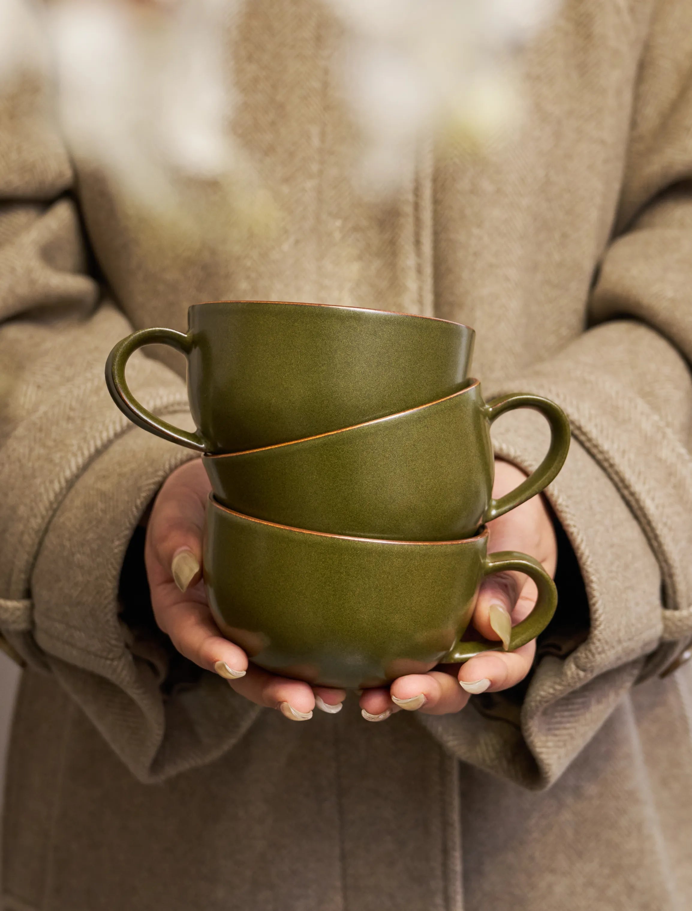 Person holding stacked SaraGaia latte mugs. Handcrafted earthy aesthetic.