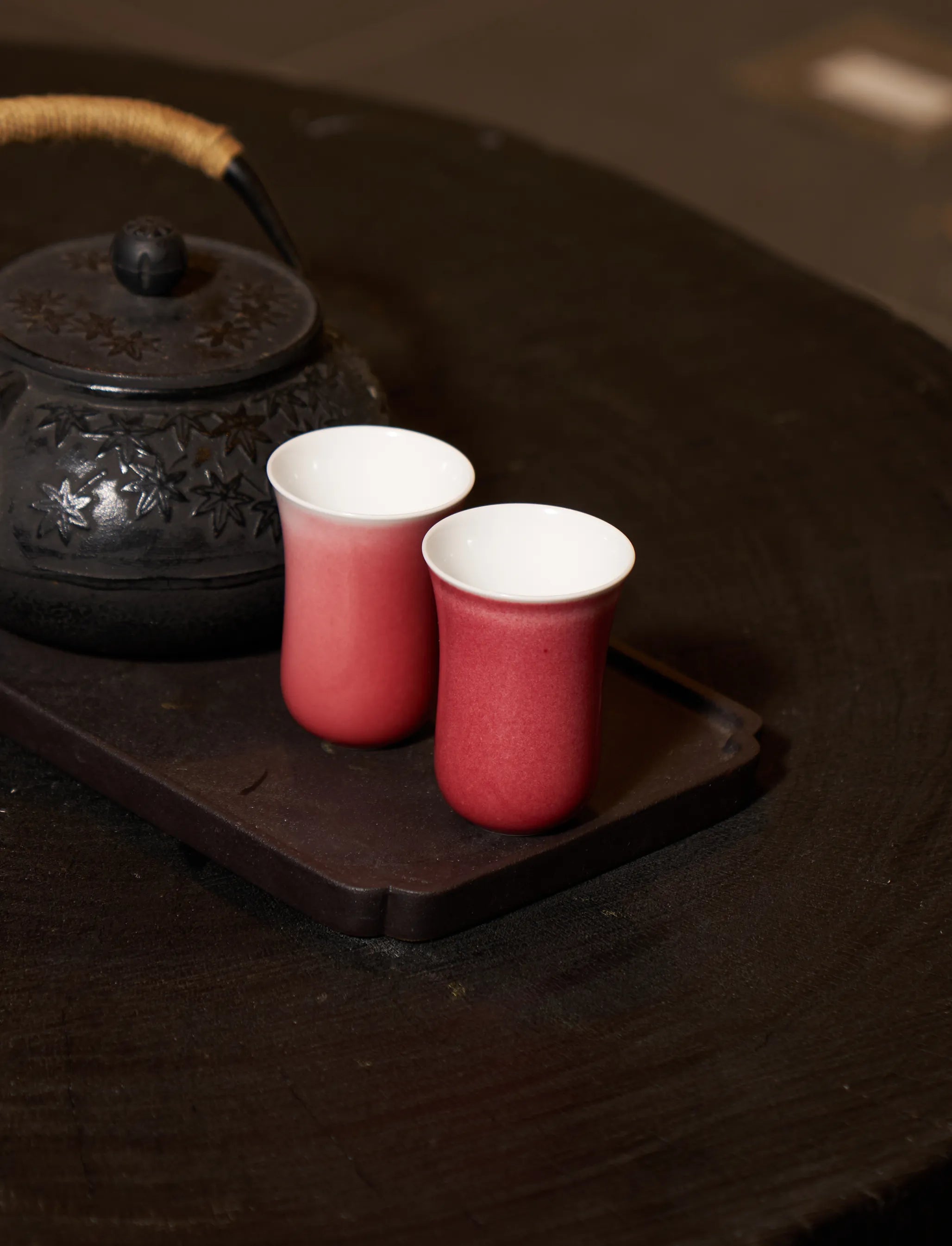 Two SaraGaia pink-red tasting cups on a dark wood tray. Zen tea ritual.