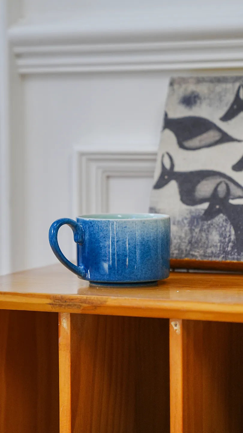SaraGaia artisan porcelain cup on a wooden shelf, showcasing minimalist home decor aesthetics.