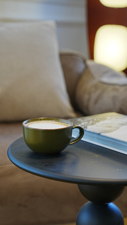 SaraGaia bamboo-shaped olive green porcelain cup on a wood stand in natural window sunlight.