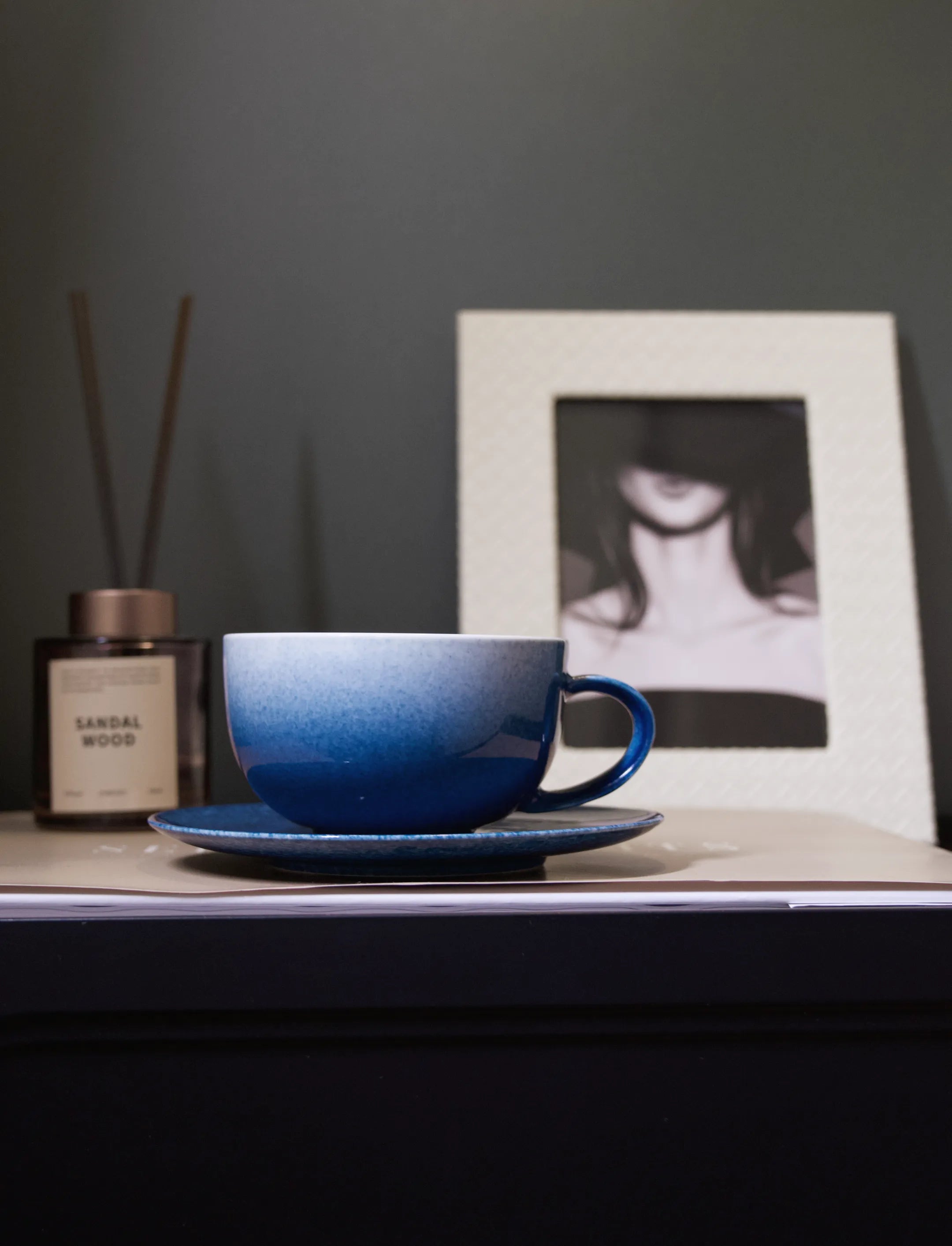 A close-up shot of a master-made Saragaia sprinkling blue ceramic latte cup and saucer set resting on a book, emphasizing its wide, rounded bowl shape and the beautiful gradient of the sprinkling blue glaze