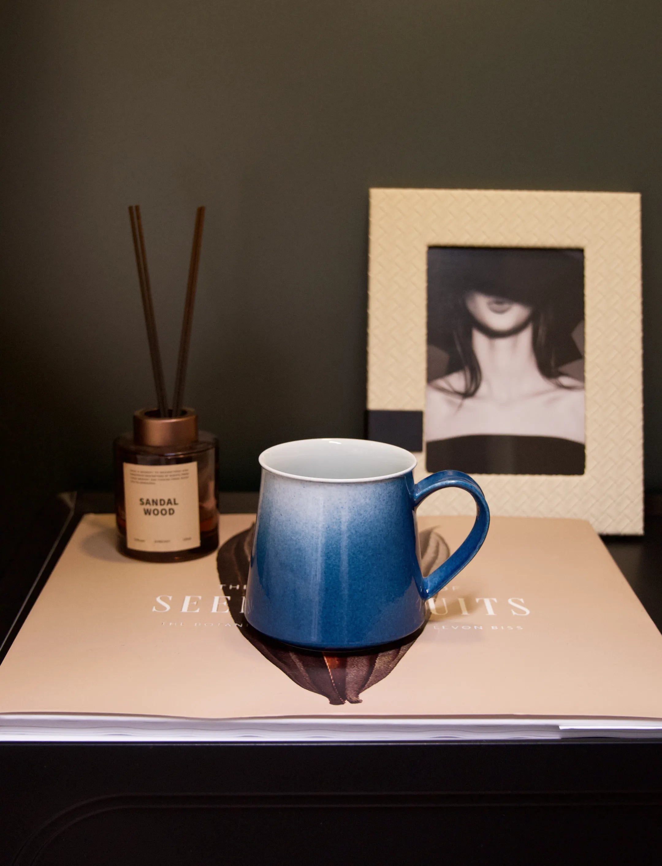 A close-up shot of a master-made Saragaia sprinkling blue ceramic mug placed on a book, highlighting its elegant trapezoidal shape and the gradient effect of the smooth, vibrant blue glaze