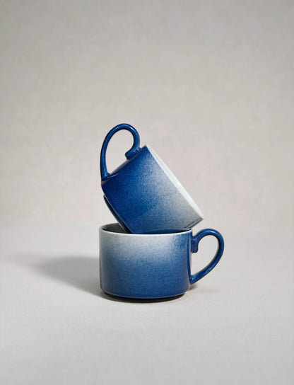 Two master-made Saragaia sprinkling blue ceramic coffee cups stacked on a neutral background
