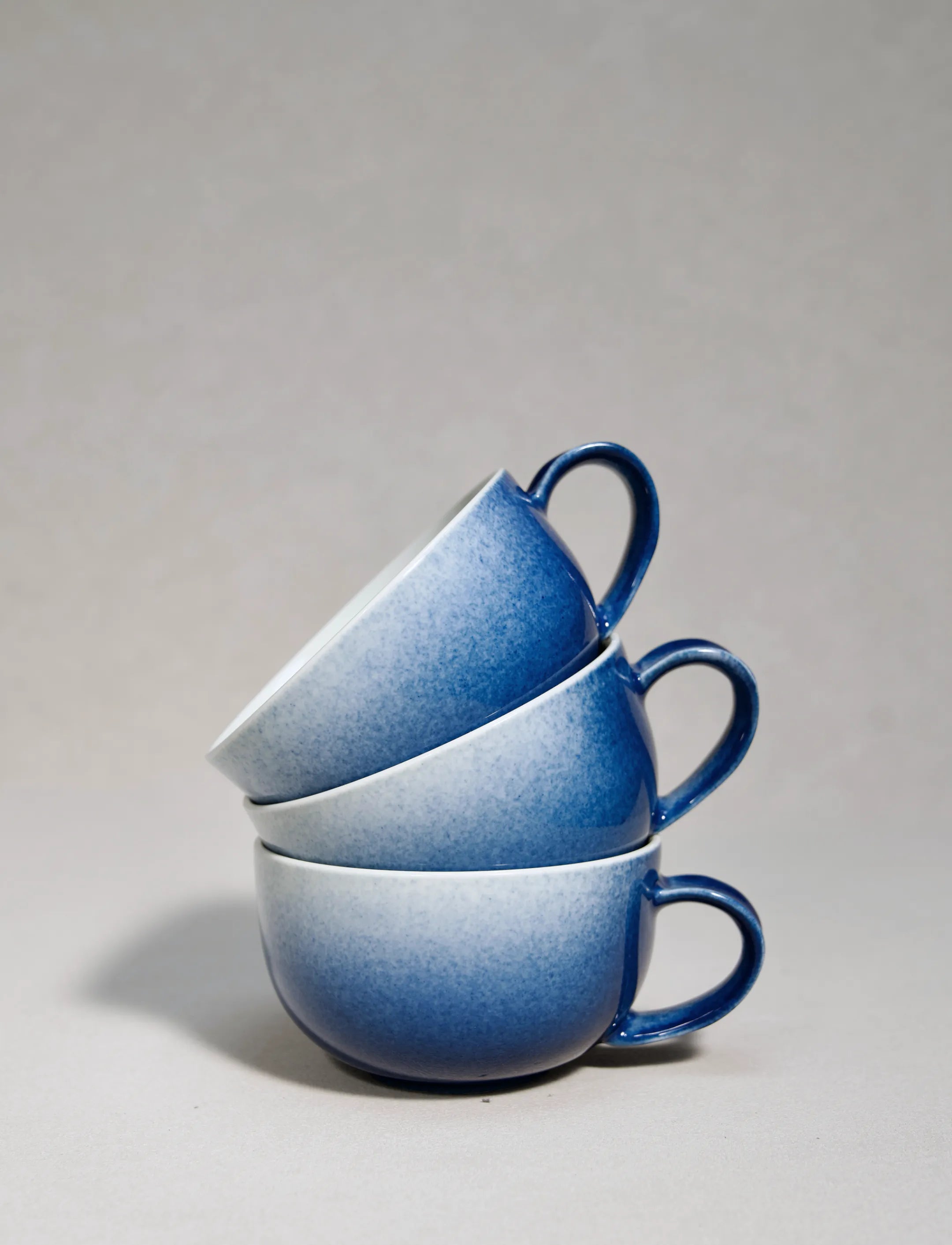 Three master-made Saragaia sprinkling blue ceramic cappuccino cups stacked on a neutral background.