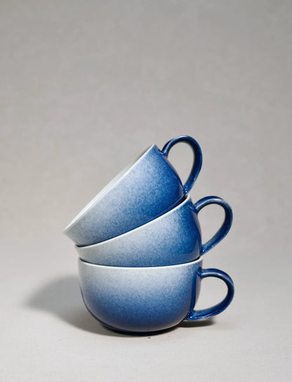 Three master-made Saragaia sprinkling blue ceramic cappuccino cups stacked on a neutral background.