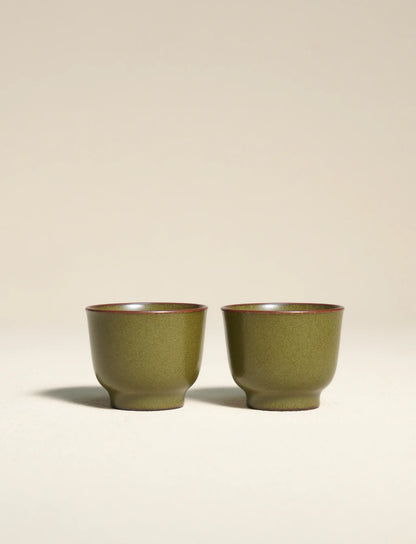 A side-by-side shot of a pair of master-made Saragaia ceramic teacups, finished in a traditional matte green tea-dust glaze with natural brown-accented rims.