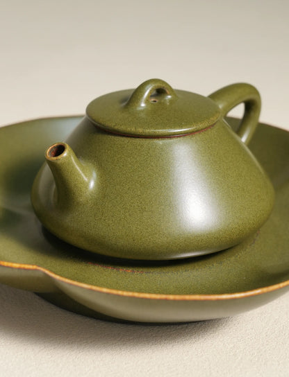 A detailed close-up shot of a master-made Saragaia ceramic teapot resting on a matching tea boat, showcasing the fine texture of the traditional matte green tea-dust glaze and the natural brown edges of the rims.
