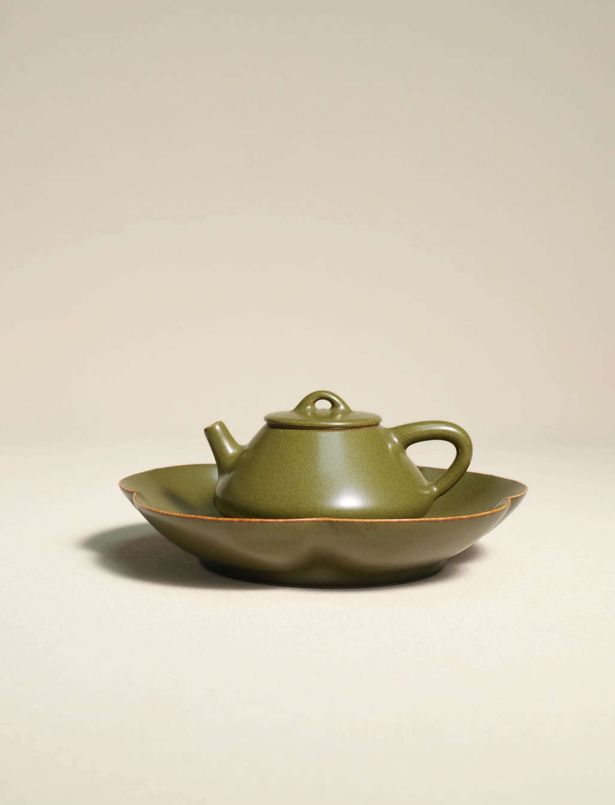 A master-made Saragaia ceramic teapot resting on a matching scalloped tea boat, finished in a traditional matte tea-dust glaze with natural brown rims.