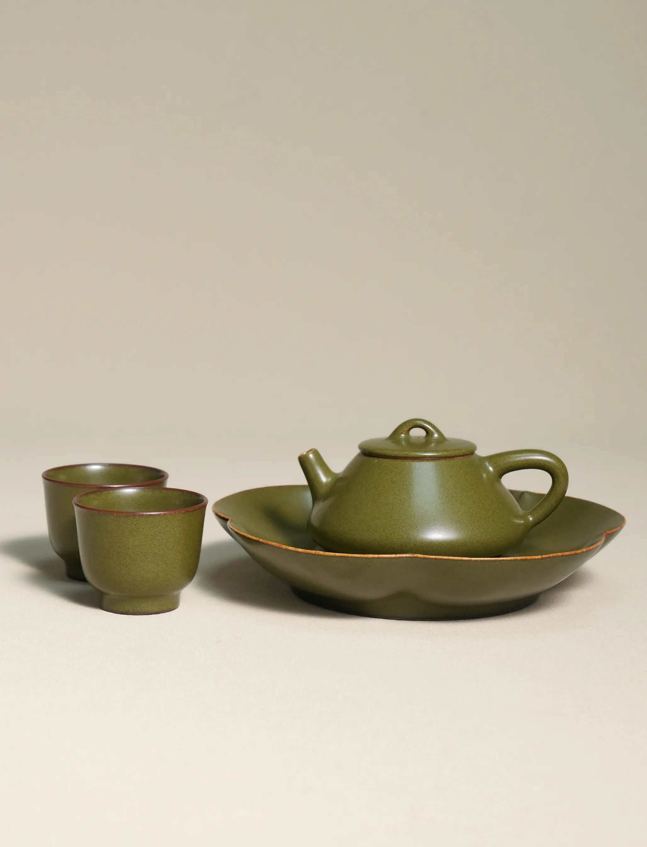 A master-made Saragaia ceramic tea set including a teapot on a scalloped tea boat alongside two matching teacups, all finished in a traditional matte green tea-dust glaze.