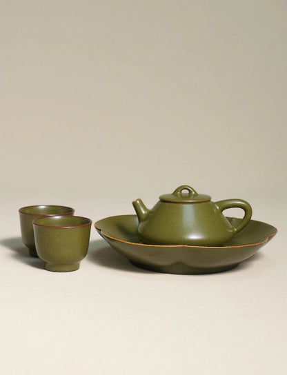 A master-made Saragaia ceramic tea set including a teapot on a scalloped tea boat alongside two matching teacups, all finished in a traditional matte green tea-dust glaze.
