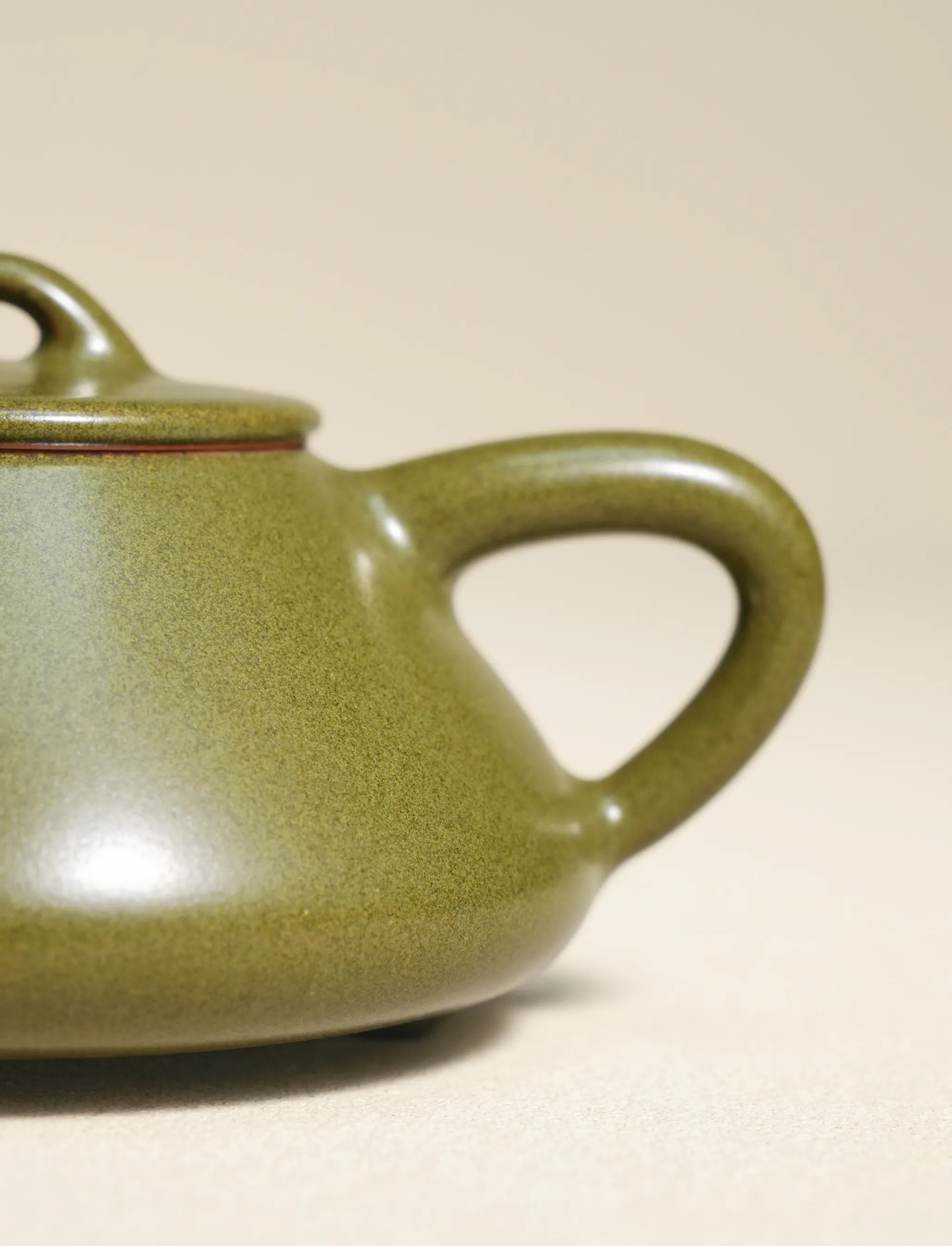 A macro close-up shot focusing on the handle and body of a master-made Saragaia ceramic teapot, highlighting the fine, speckled texture of the traditional matte green tea-dust glaze.