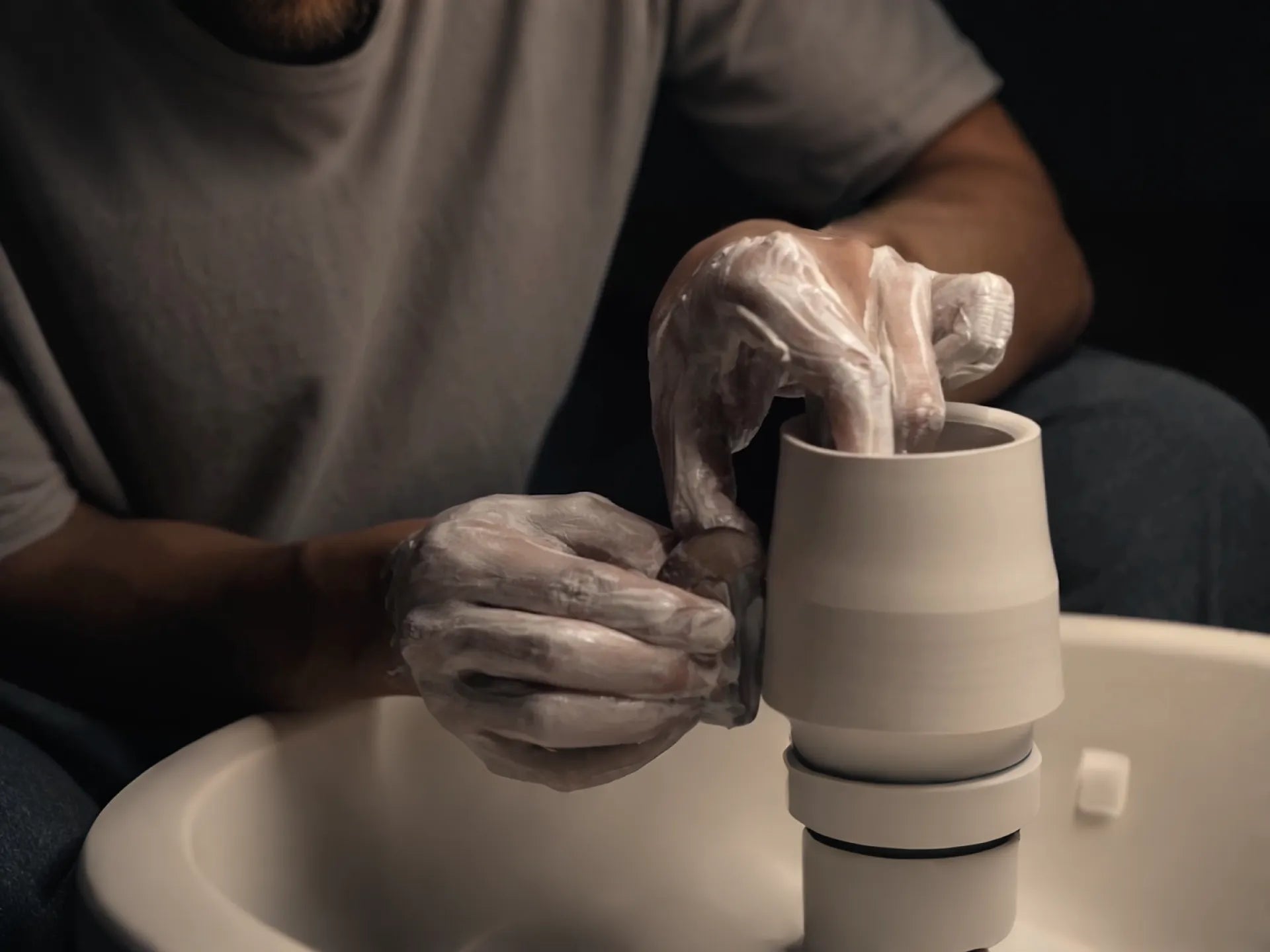 A master potter, heavily covered in glaze, skillfully shapes a cup on a pottery wheel for Saragaia Jingdezhen.