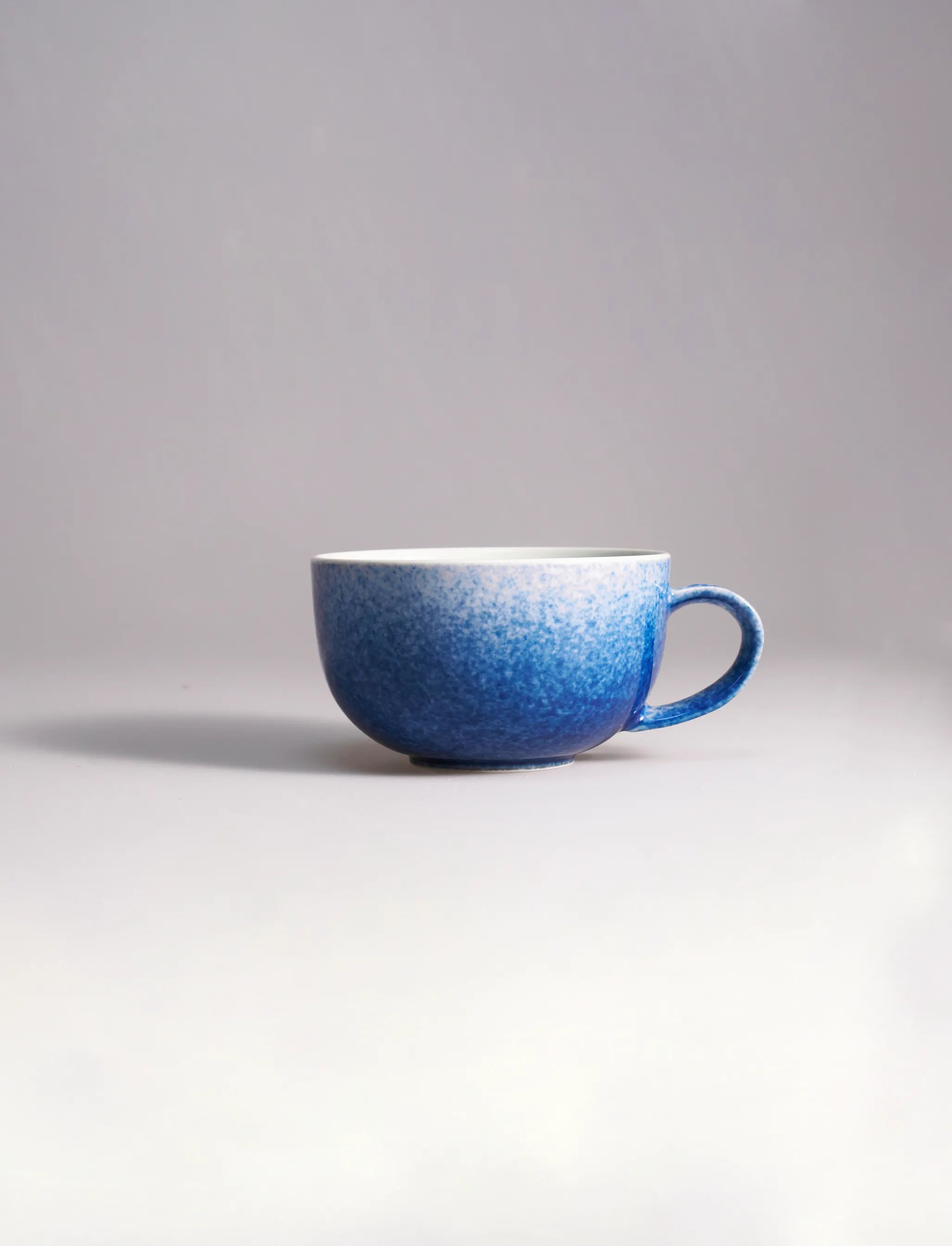 SaraGaia artisan porcelain cup featuring a gradient sprinkling blue snowflake glaze effect.